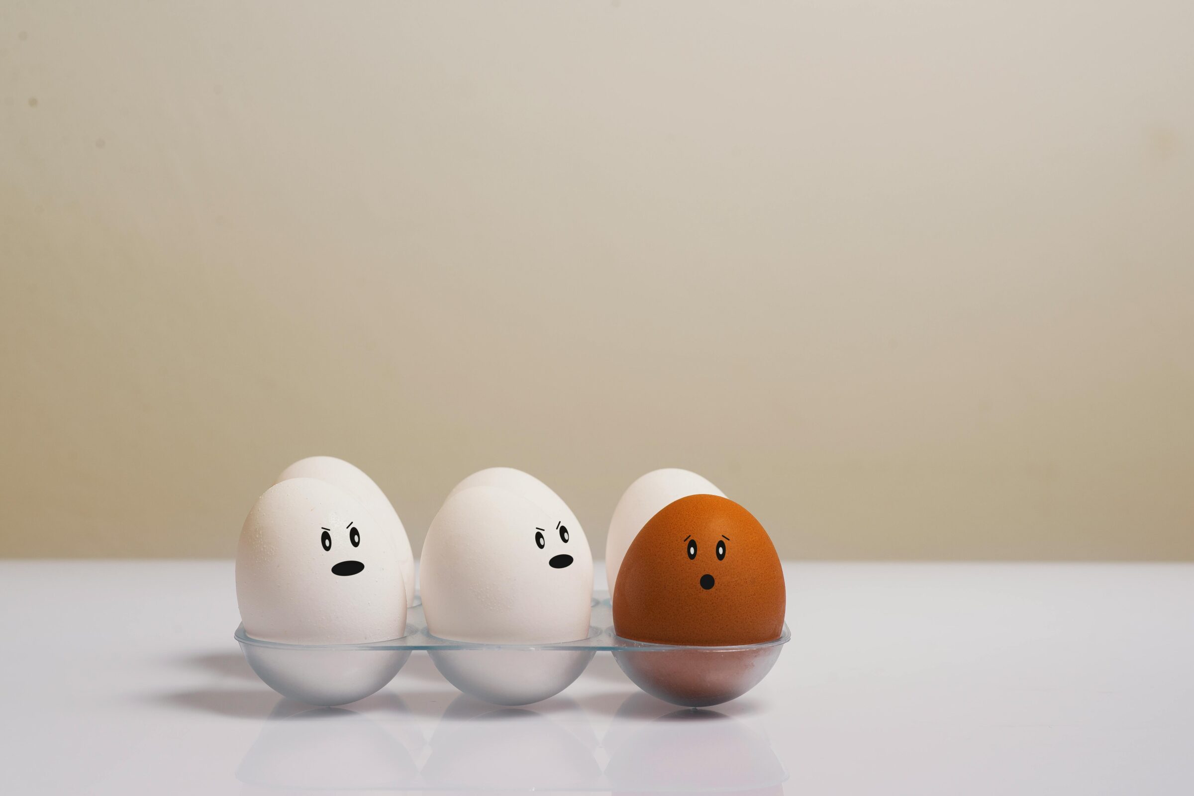 one brown egg and five white eggs in carton on white table top