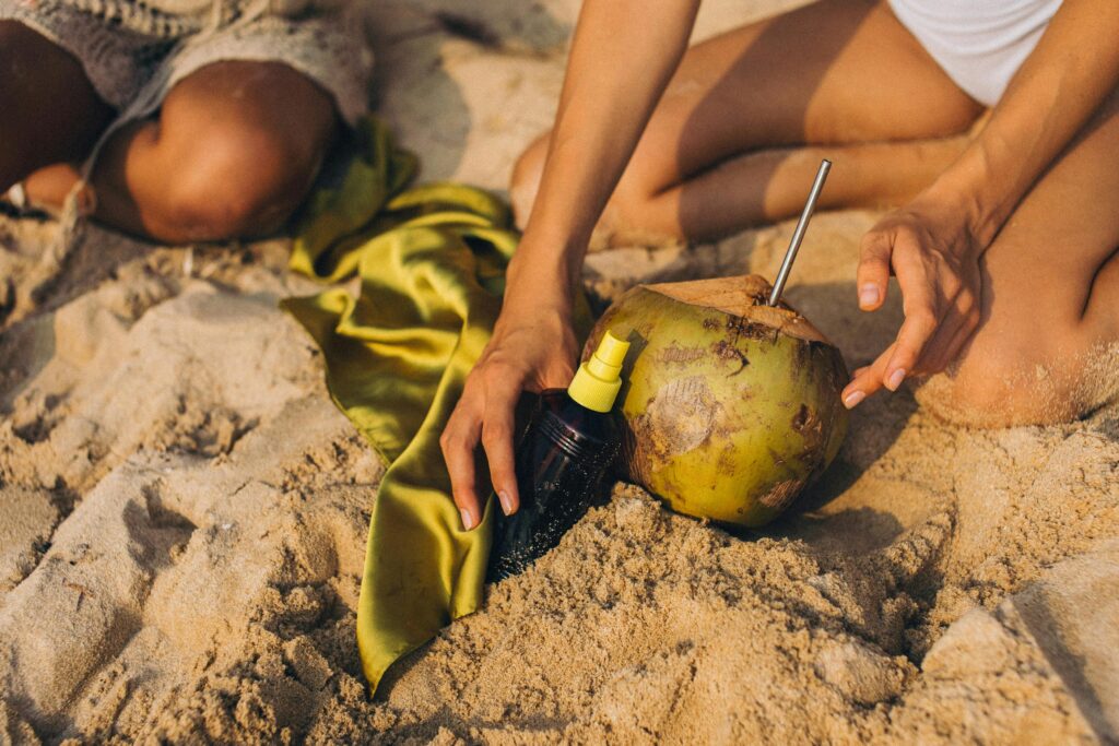 spray bottle in sand next to coconut